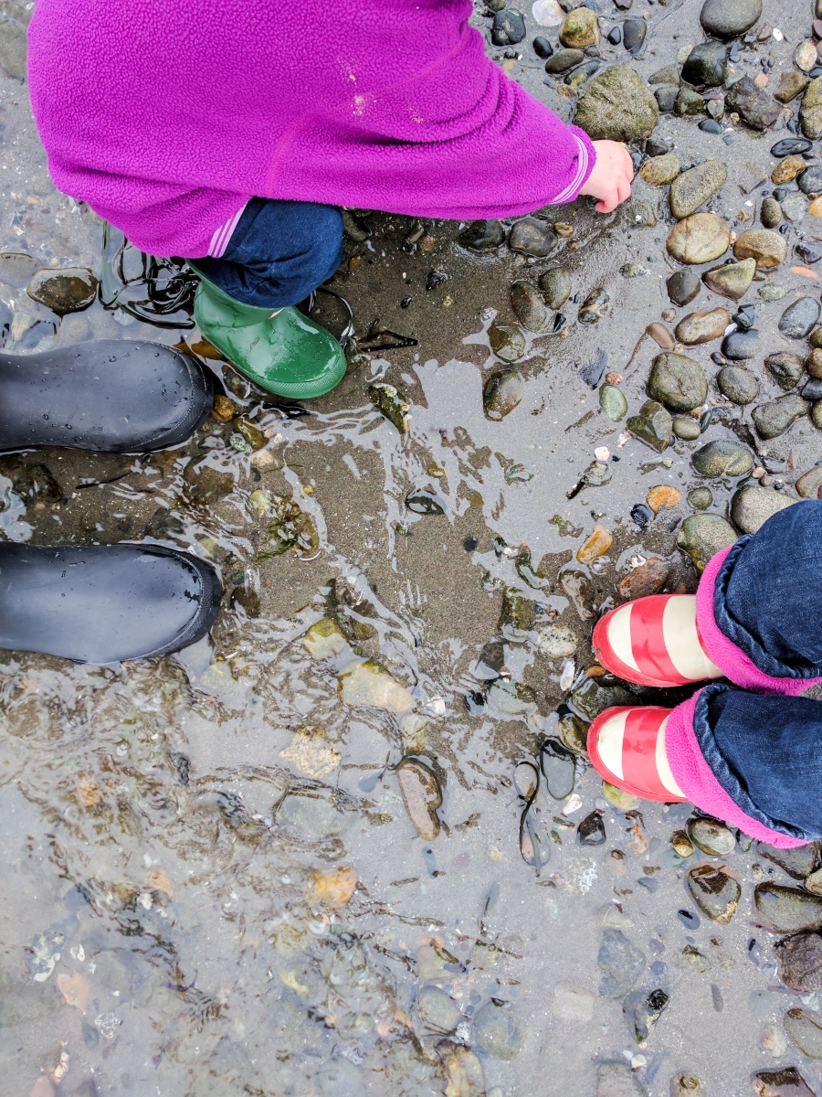 anxiety: pier stretching out to the ocean, close up of three pairs of rubber boots in the ocean water and standing on rocks.